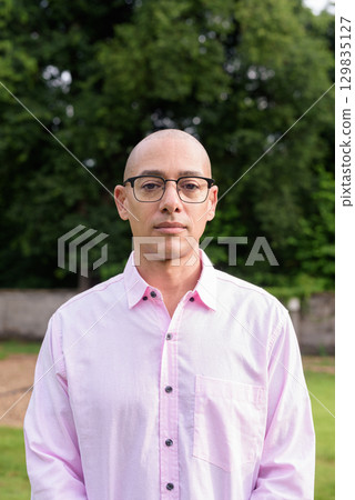 Bald Hispanic man wearing pink casual business shirt and eyeglasses outdoors 129835127