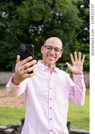 Bald Hispanic man wearing pink casual business shirt and eyeglasses outdoors 129835150