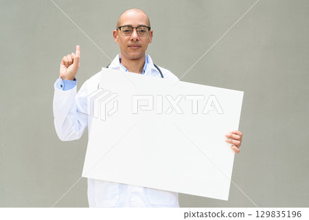 Hispanic Male Doctor in Lab Coat with Stethoscope on Plain Background Holding Empty Placard Hispanic Male Doctor in Lab Coat with Stethoscope on Plain Background Holding Empty Placard 129835196
