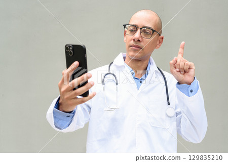 Hispanic Male Doctor in Lab Coat with Stethoscope on Plain Background Using Phone Hispanic Male Doctor in Lab Coat with Stethoscope on Plain Background Using Phone 129835210