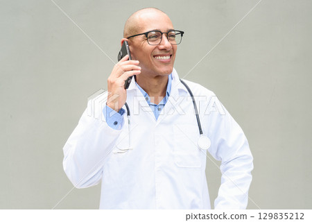 Hispanic Male Doctor in Lab Coat with Stethoscope on Plain Background Talking on Phone Hispanic Male Doctor in Lab Coat with Stethoscope on Plain Background Talking on Phone 129835212