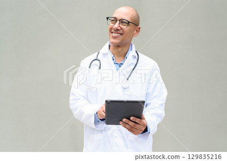 Hispanic Male Doctor in Lab Coat with Stethoscope on Plain Background Using Tablet Computer 129835216