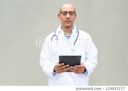 Hispanic Male Doctor in Lab Coat with Stethoscope on Plain Background Using Tablet Computer 129835217