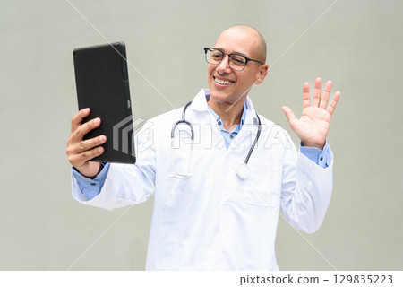 Hispanic Male Doctor in Lab Coat with Stethoscope on Plain Background Using Tablet Computer Hispanic Male Doctor in Lab Coat with Stethoscope on Plain Background Using Tablet Computer 129835223