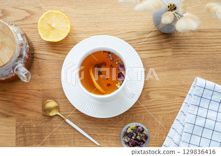 A cup of herbal tea with lemon, napkin and dry bouquet of flowers on a wooden table 129836416