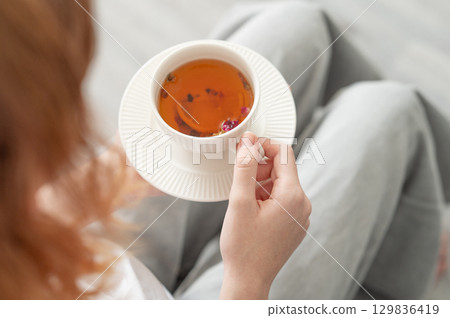 Woman holding white cup of tea with lemon and herbs in cozy bright room. Woman holding white cup of tea with lemon and herbs in cozy bright room. 129836419
