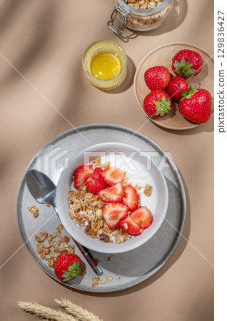 Granola or muesli with natural greek yogurt, strawberry and honey in a bowl on a beige background Granola or muesli with natural greek yogurt, strawberry and honey in a bowl on a beige background 129836427