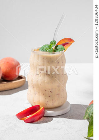 Smoothie with peach and banana in a glass on a marble stand on a light background Smoothie with peach and banana in a glass on a marble stand on a light background 129836434