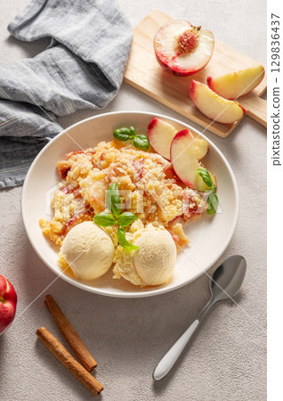 Peach crumble or cobbler with vanilla ice cream scoops and cinnamon on a plate on a light background Peach crumble or cobbler with vanilla ice cream scoops and cinnamon on a plate on a light background 129836437