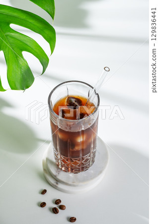 Cold brew coffee tonic in a glass with ice on a light background with coffee beans, monstera 129836441