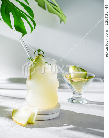 Cold lemonade or mojito in a glass with melon, straw and mint on a light background with pieces  129836444