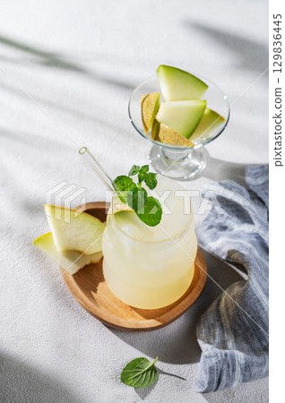 Refreshing lemonade or mojito in a glass with melon, straw and mint on a wooden plate  129836445