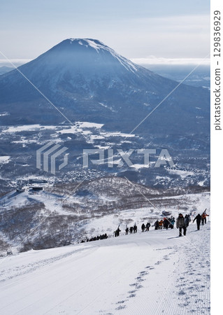 People climbing from Niseko Tokyu Grand Hirafu slope to Niseko Annupuri outside the ski resort management area with Mt. Yotei in the background 129836929