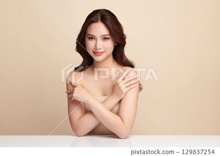 A beautiful young Asian woman with clean, fresh skin against a beige background. Skincare, facial treatment, cosmetology, beauty, and spa. An elegant portrait of an Asian woman. 129837254