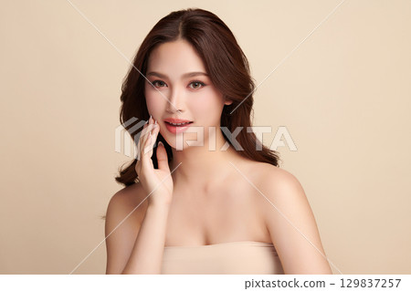 A beautiful young Asian woman with clean, fresh skin against a beige background. Skincare, facial treatment, cosmetology, beauty, and spa. An elegant portrait of an Asian woman. A beautiful young Asian woman with clean, fresh skin against a beige background. Skincare, facial treatment, cosmetology, beauty, and spa. An elegant portrait of an Asian woman. 129837257