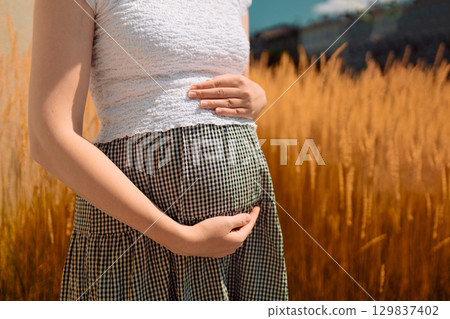 Pregnant Woman Holding Belly in Golden Wheat Field 129837402