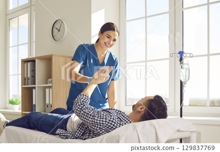 Nurse giving high five to man receiving IV drip infusion and vitamin therapy in medical clinic 129837769