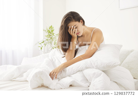 Unhappy young Caucasian woman sitting in bed, feeling unwell after night and unwilling to get up. Unhappy young Caucasian woman sitting in bed, feeling unwell after night and unwilling to get up. 129837772