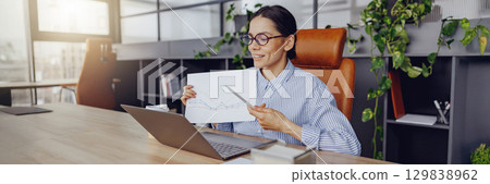 A Professional Woman Focused on Her Work at an Office Desk Surrounded by Presentation Materials 129838962