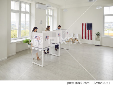 American citizens standing at vote center in voting booth at polling station on election day. 129840047