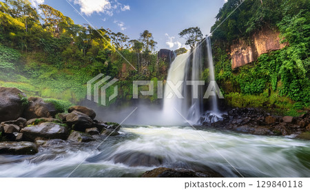 roaring waterfall crashing into rocks, surrounded by lush greenery 129840118
