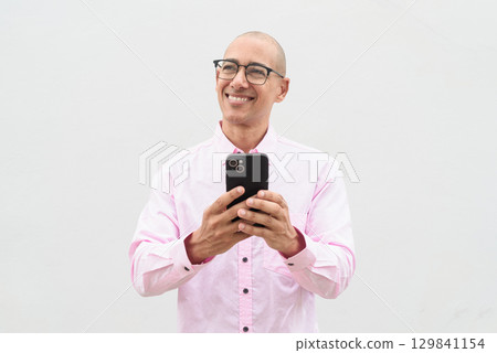 Happy bald man using phone texting sms message against white background 129841154