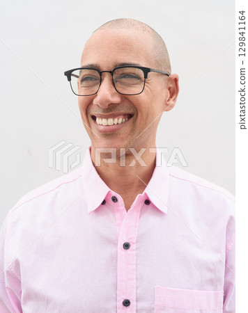 Happy bald Hispanic face man wearing pink casual business shirt and eyeglasses while thinking 129841164
