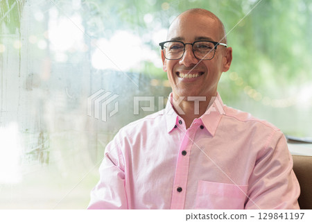 Bald Hispanic man wearing pink casual business shirt and eyeglasses in coffee shop cafe restaurant 129841197