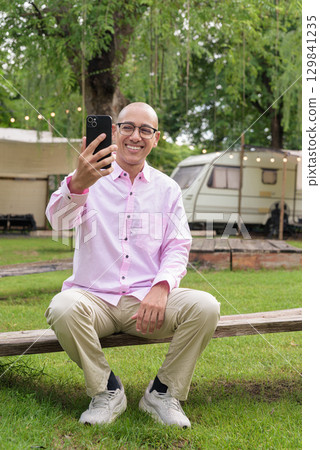 Full length portrait of bald Hispanic man outdoors using phone in park Full length portrait of bald Hispanic man outdoors using phone in park 129841235