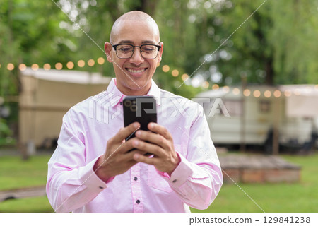 Bald Hispanic man wearing pink casual business shirt and eyeglasses outdoors using phone Bald Hispanic man wearing pink casual business shirt and eyeglasses outdoors using phone 129841238
