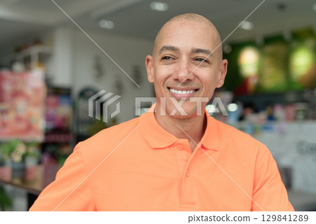 Bald Hispanic man happy smiling face inside cafe restaurant wearing orange polo shirt Bald Hispanic man happy smiling face inside cafe restaurant wearing orange polo shirt 129841289