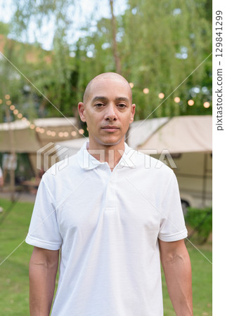 Bald man relaxing at campsite with camper van in outdoor travel lifestyle scene looking at camera Bald man relaxing at campsite with camper van in outdoor travel lifestyle scene looking at camera 129841299