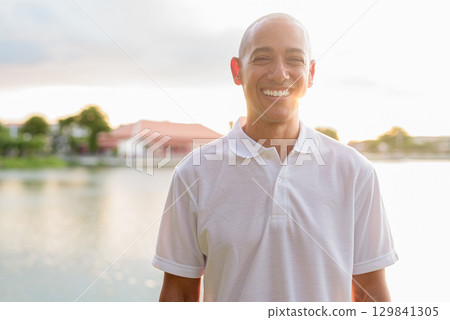 Summer portrait of bald man face headshot next to park lake during sunset with lens flare 129841305