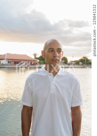 Summer portrait of bald man next to park lake during sunset with lens flare Summer portrait of bald man next to park lake during sunset with lens flare 129841312