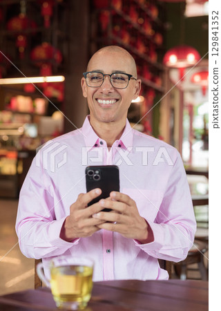 Bald Hispanic man wearing pink casual business shirt and eyeglasses in Chinese style tea house 129841352