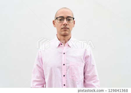 Bald Hispanic man wearing pink casual business shirt and eyeglasses against white background 129841368