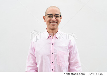 Bald Hispanic man wearing pink casual business shirt and eyeglasses against white background 129841369