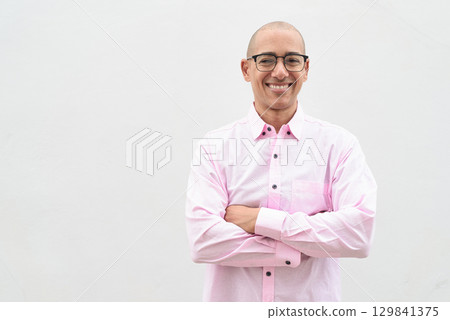 Bald Hispanic man wearing pink casual business shirt and eyeglasses against white background 129841375