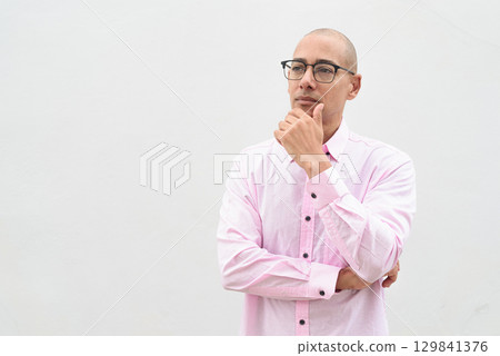 Bald Hispanic man wearing pink casual business shirt and eyeglasses thinking and looking up 129841376
