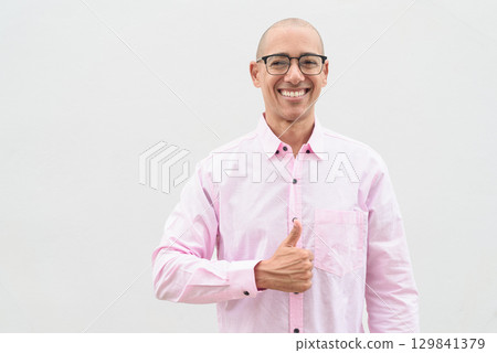 Bald Hispanic man wearing pink casual business shirt and eyeglasses with thumb up gesture Bald Hispanic man wearing pink casual business shirt and eyeglasses with thumb up gesture 129841379