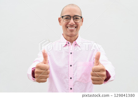Bald Hispanic man wearing pink casual business shirt and eyeglasses with thumb up gesture Bald Hispanic man wearing pink casual business shirt and eyeglasses with thumb up gesture 129841380