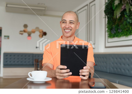 Bald Hispanic man using digital tablet computer in coffee shop 129841400