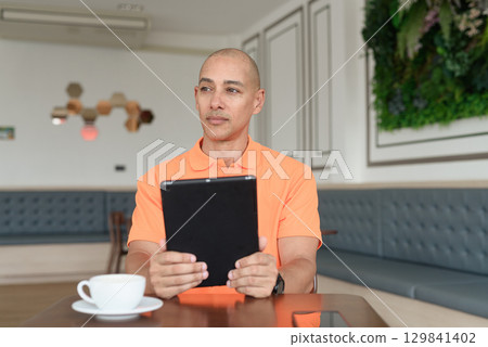 Bald Hispanic man using digital tablet computer in coffee shop Bald Hispanic man using digital tablet computer in coffee shop 129841402