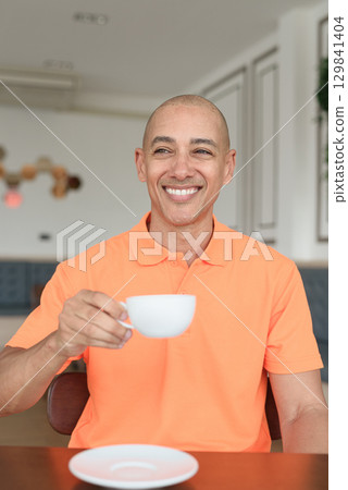 Happy man holding coffee cup inside cafe restaurant wearing orange polo shirt Happy man holding coffee cup inside cafe restaurant wearing orange polo shirt 129841404