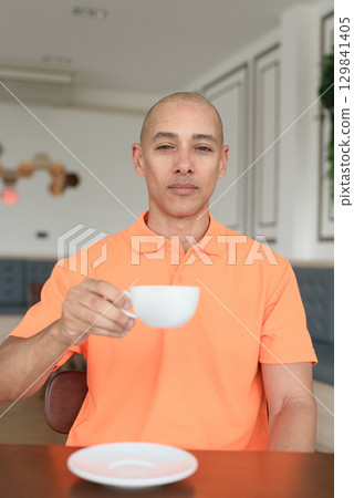 Man holding coffee cup inside cafe restaurant wearing orange polo shirt 129841405