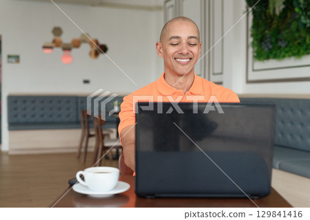 Happy bald Hispanic man smiling and using laptop computer in coffee shop restaurant 129841416