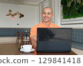 Bald Hispanic man smiling and using laptop computer in coffee shop restaurant while thinking 129841418