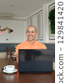 Bald Hispanic man smiling and using laptop computer in coffee shop restaurant while thinking 129841420