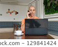 Bald Hispanic man using laptop computer in coffee shop restaurant while talking on phone 129841424