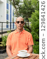 Bald Hispanic man face sitting outdoors at cafe restaurant wearing orange polo shirt 129841426